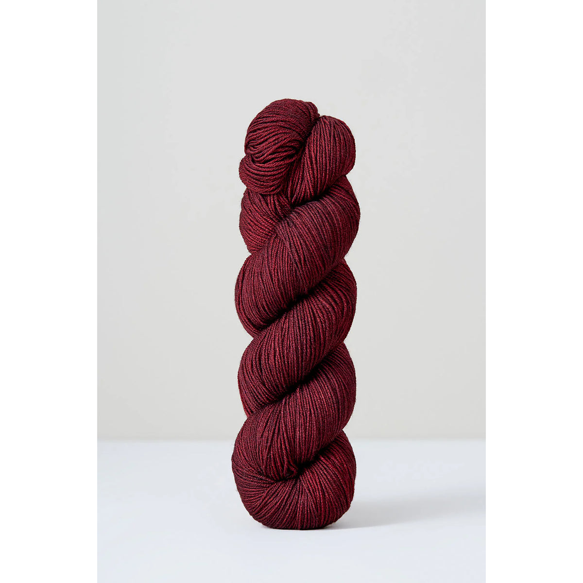 A skein of Urth Harvest Fingering Black Grape, a deep, rich wine red color.