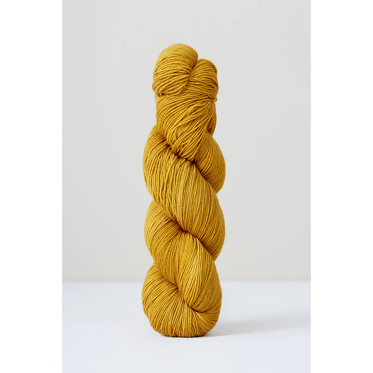 A skein of Urth Harvest Fingering Buckthorn, a golden, dark mustard yellow color.