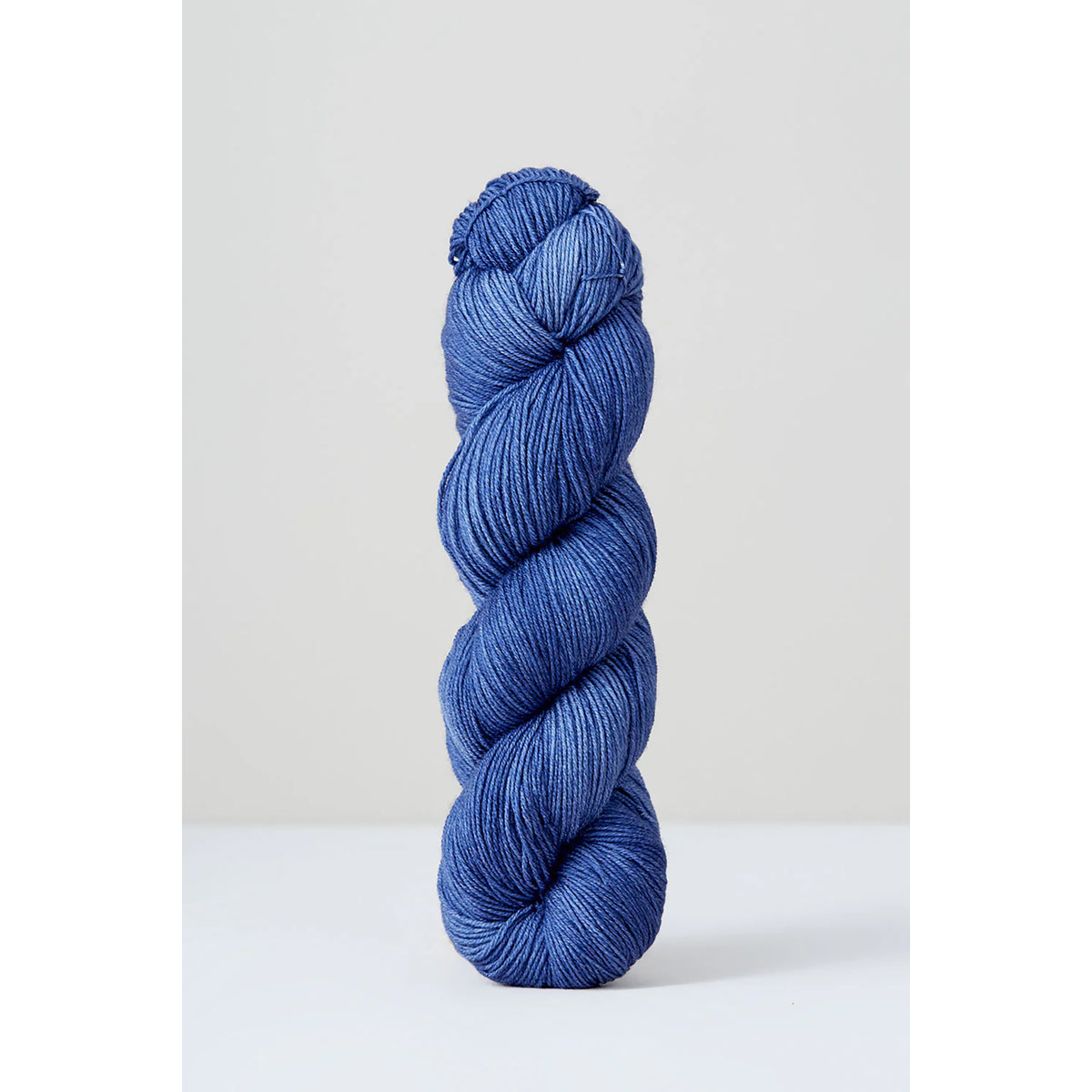 A skein of Urth Harvest Fingering Cosmic Purple Carrot, a cornflower blue color with grey undertones.