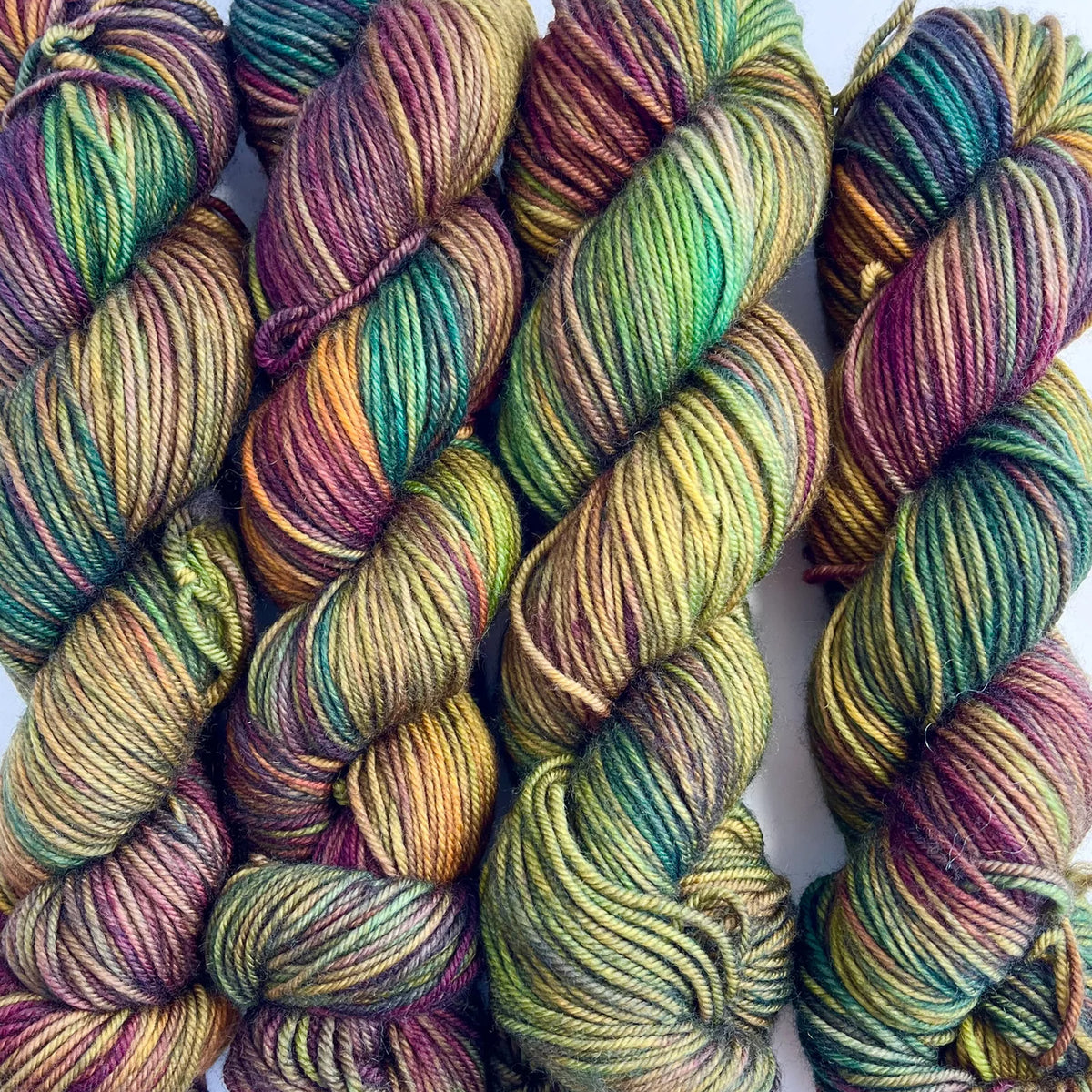 Skeins of Tributary Tidal DK Maple Leaf, variegated light green, burgundy, leaf green, with hints of yellow and brown