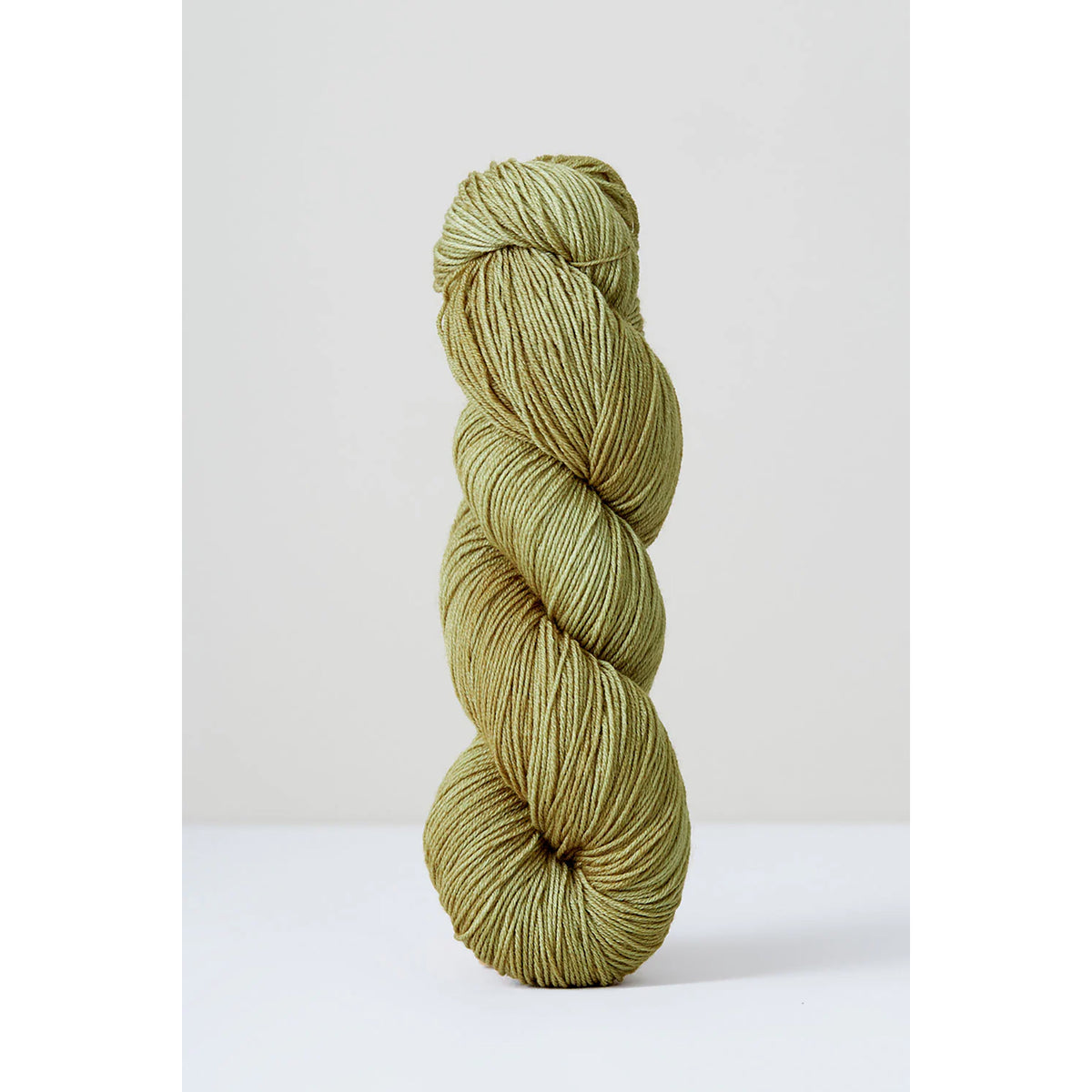 A skein of Urth Harvest Fingering Pistachio, a pale grassy green color.