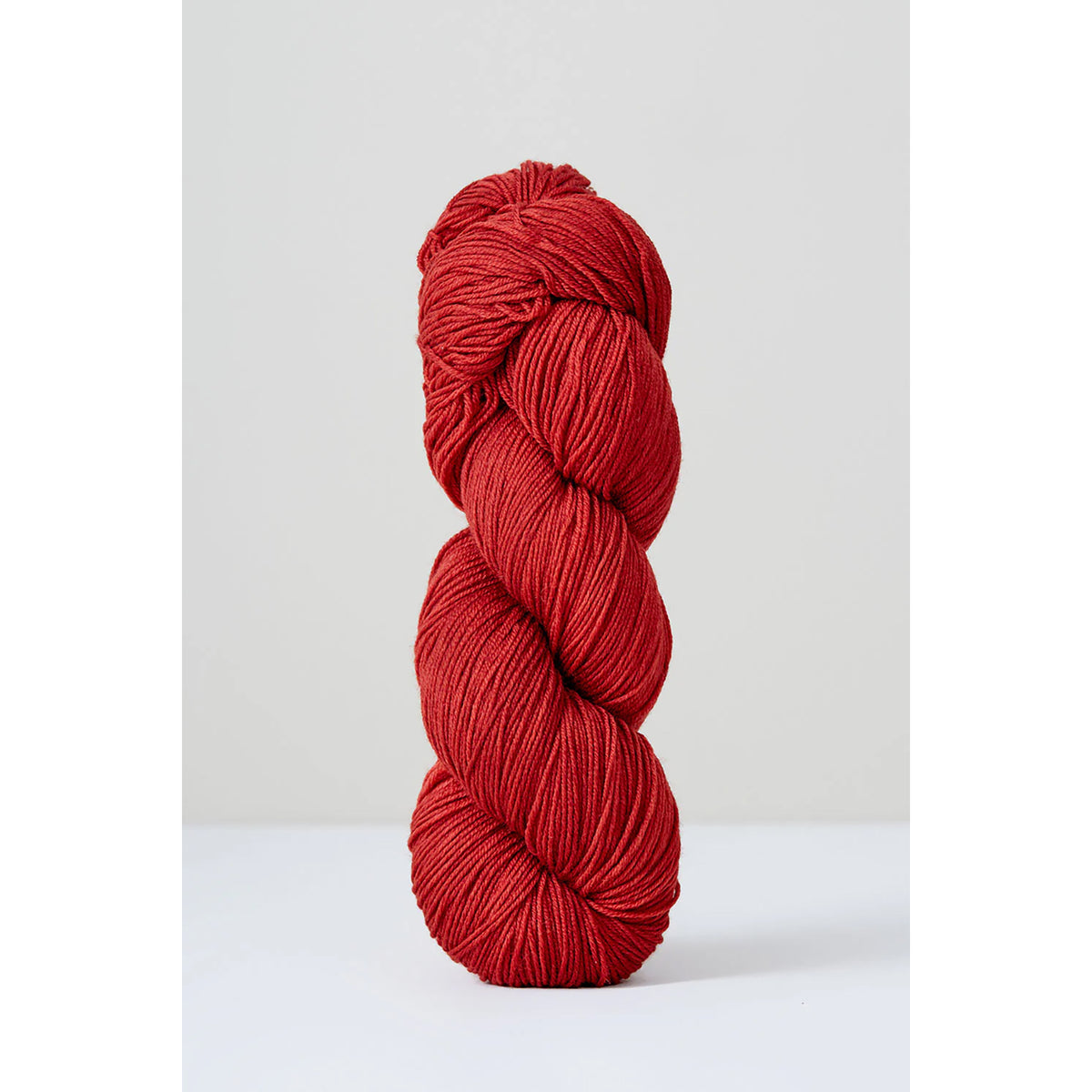 A skein of Urth Harvest Fingering Rubia, an earthy red color.