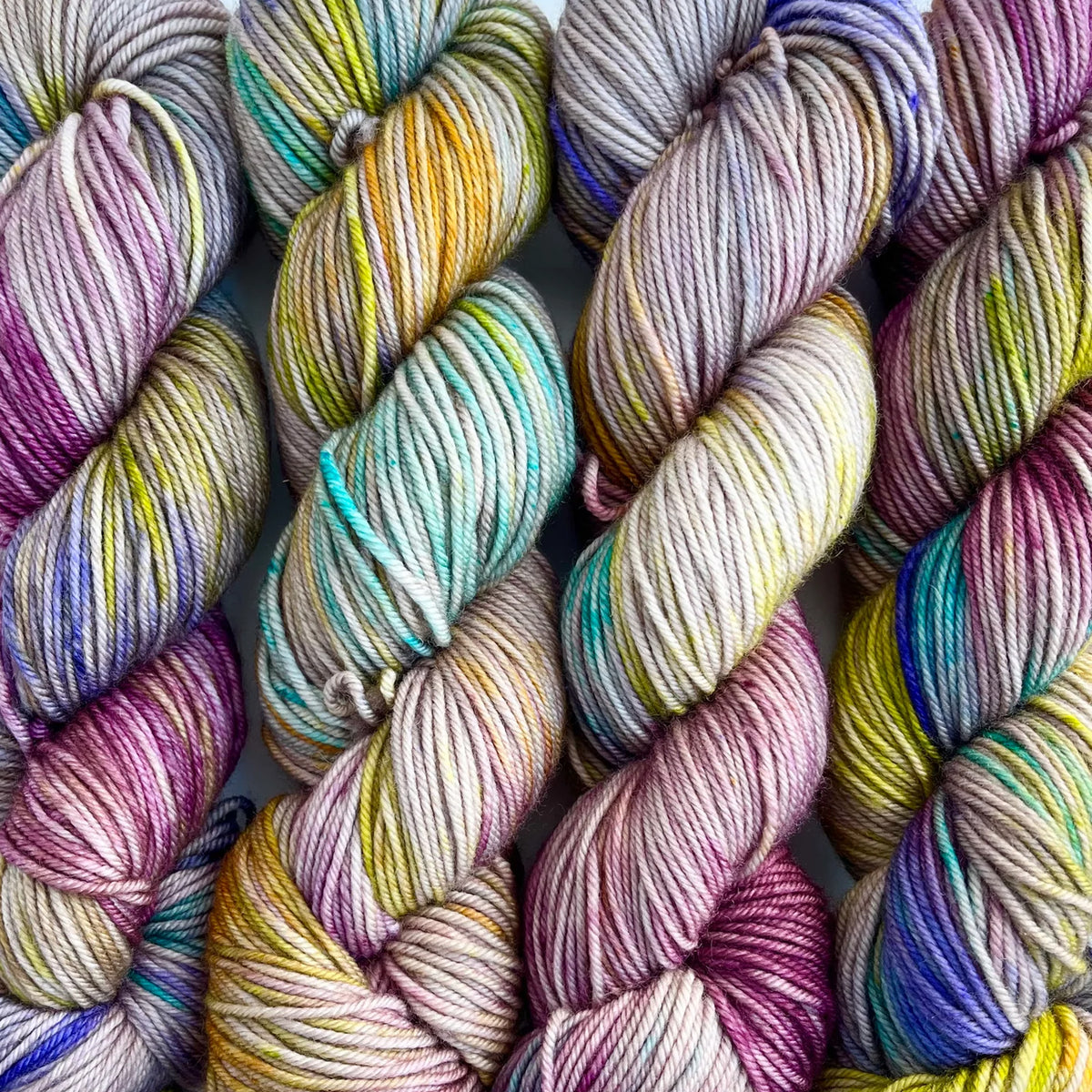 Skeins of Tributary Tidal DK Stonefly, variegated greys, muted yellows, teal, and dark magenta