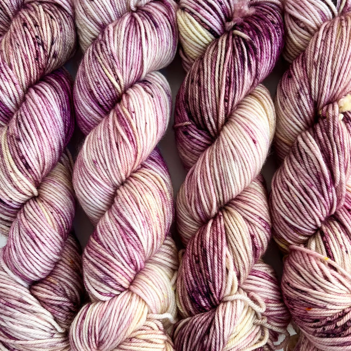 Skeins of Tributary Tidal DK Wren, a variegated buttercream and plum color with dark speckles 