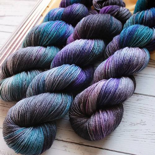 Yarn Love Amy Oil Slick a variegated yarn in turquoise, royal blue, purple and dark grey.
