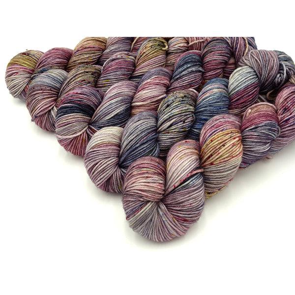 Skeins of Murky Depths Neptune DK Holi, Interrupted, a variegated yarn in muted shades of yellow, navy, rose and cream. 